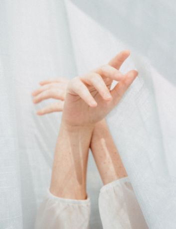 twee armen die omhoog wijzen met gekruiste handen voor een zacht wit gordijn